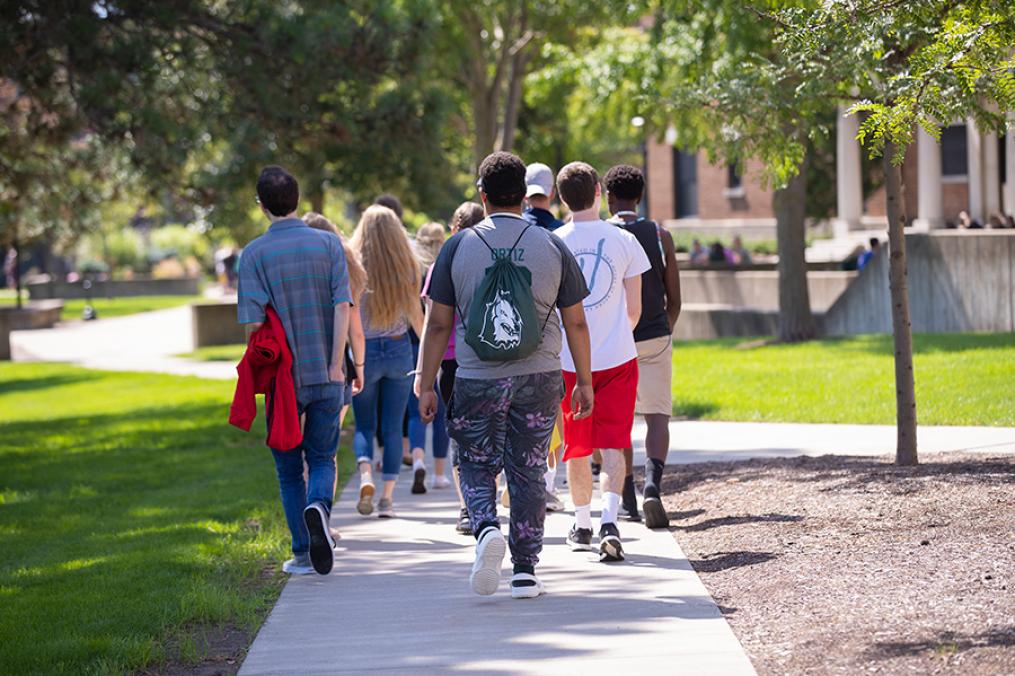 Students walking across the campus. One student is wearing a KC Wolves backpack.